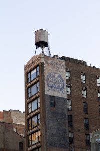 American Odyssey shows a 35mm digital colour image of part of a New York office building with a rooftop water tank typical of the city.