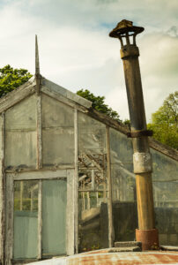 A 35mm digital colour image of an old chimney stack with an old glasshouse in the background in the walled garden of Russborough House.