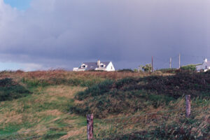 A 35mm Kodak Ektar colour film image looking from the coastline of the Dingle Peninsula inland to a bungalow in the midst of low lying vegetation