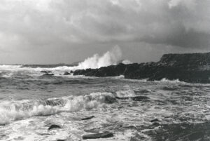 A 35mm black and white film photograph of rough sea and high waves beating off rocks at Winestrand