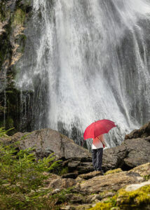 A 35mm digital colour photographic image of the famous Powerscourt Waterfall in all its glory with a lady holding a red umbrella.