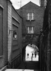 New Photos shows a 35mm Ilford XP2 black and white film image of a lane and old archway very near Dublin Castle and some people walking on the other side of the Archway